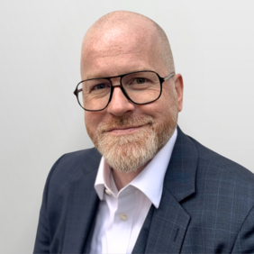 Ole Kopitz - Executive Vice President Sales & Marketing and Managing Director Ein Mann mit Glatze und Bart trägt eine dunkle Jacke und ein helles Hemd. Er lächelt freundlich in die Kamera vor einem hellen Hintergrund. Seine Brille hat ein modernes Design.