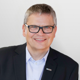 Christof Schmeer - Vice President Quality & Regulatory Affairs A smiling middle-aged man with short gray hair and black glasses is wearing a dark blazer over a light blue shirt. He appears friendly and approachable, with a neutral light background. A small name tag is visible on his blazer.