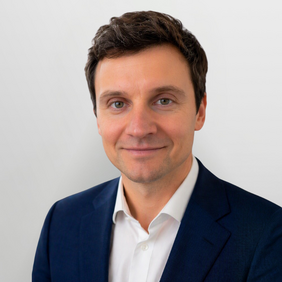 Christian Jost - Vice President Regulatory Affairs & Quality Management Ein Mann mit kurzen, braunen Haaren und einem freundlichen Lächeln trägt einen dunkelblauen Anzug und ein weißes Hemd. Der Hintergrund ist hell und schlicht.
